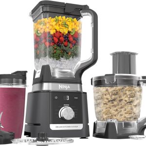 Ninja CO905KS Deluxe Kitchen System with 1600-Watt Auto-iQ Base, blender pitcher filled with fruit and ice, food processor bowl with dough, two 24-oz smoothie cups, and multiple blade attachments.